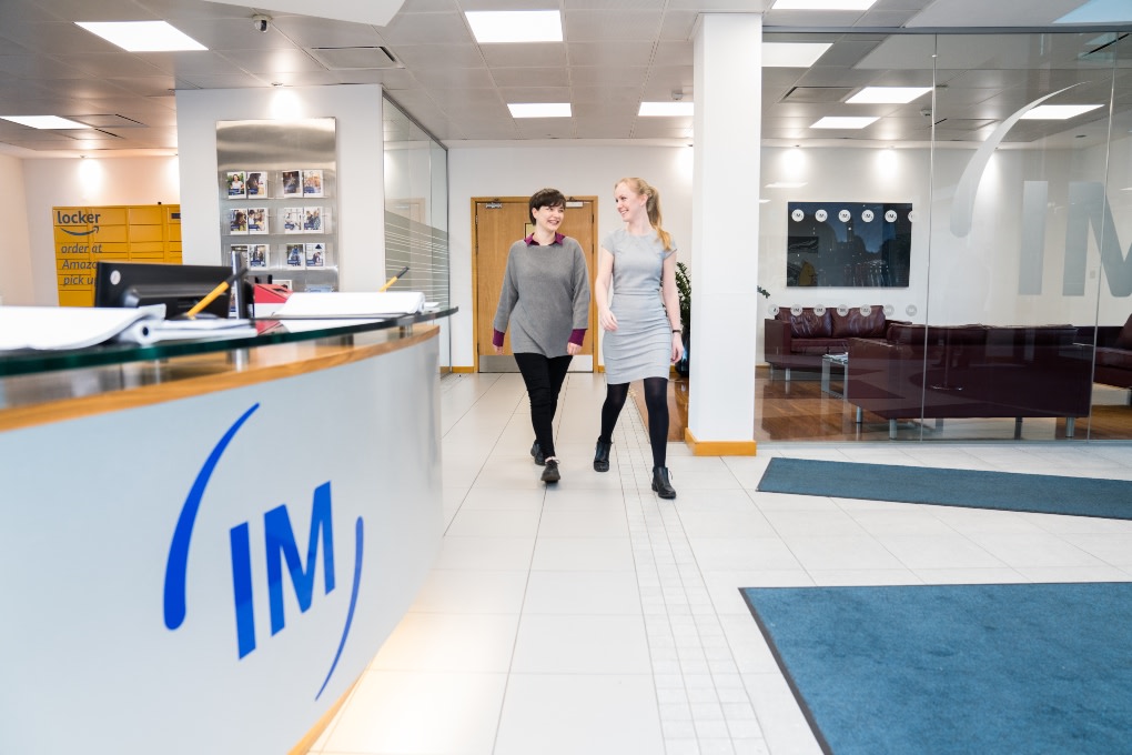 Two people smiling while walking past Irwin Mitchell reception desk